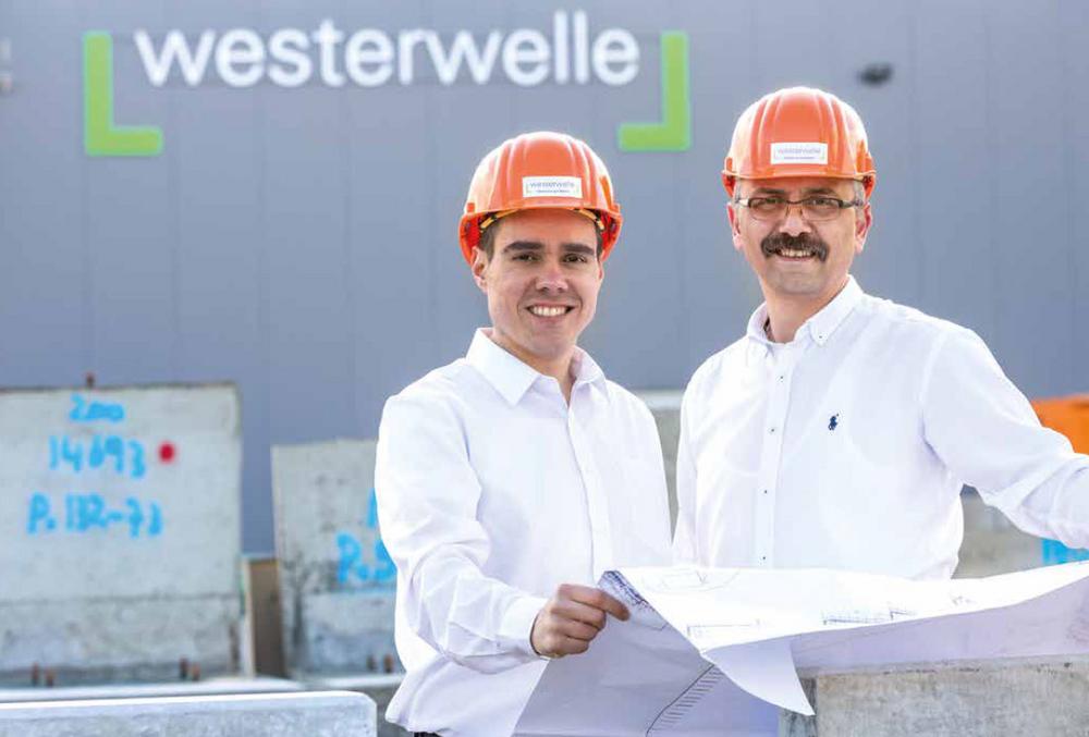 [Translate to Polski:] Zwei Mitarbeiter mit Helmen und Bauplan vor Westerwelle-Gebäude